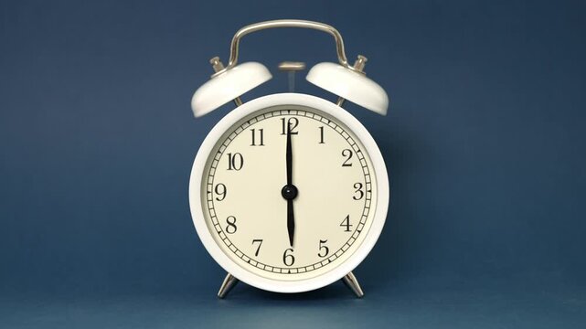 Classic white twin bell alarm clock sounding loudly at six in the morning on a deep blue background, signaling it's time to wake up and start the day with a sense of urgency and routine