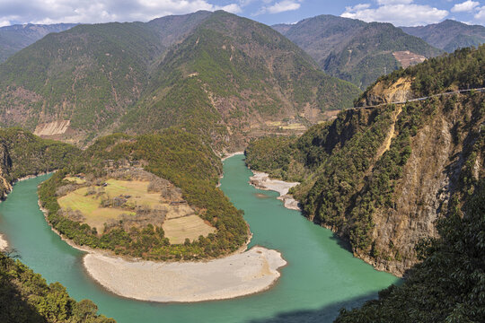 View of the Nujiang River's first bend, a ribbon of turquoise slicing through the rugged, forested mountains under a vast sky, First bend of Nujiang River, China.