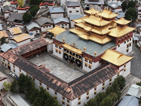 Aerial view of a golden-roofed monastery stands majestically amidst a sea of white buildings, its intricate architecture a beacon of serenity, Dongzhulin, Yunnan, China.