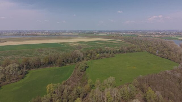 An expansive view showcases the beauty of a vast landscape featuring a mosaic of textures. Lush fields intertwine with lines of trees beneath a tranquil sky.
