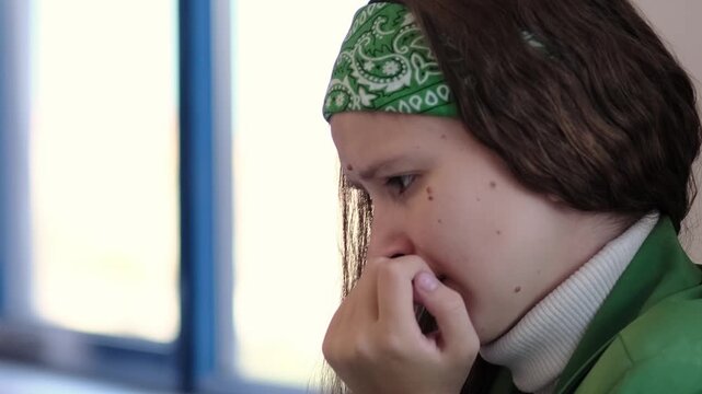 A teenage girl clutches her hand tightly to her face, her expression filled with concern and unease. The scene represents anxiety, emotional distress, and the difficulty of coping with overwhelming