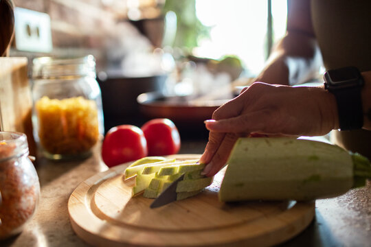 Person slicing zucchini on a cutting board in a home kitchen