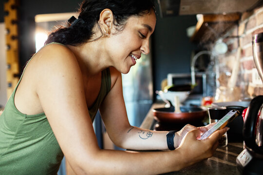 Smiling woman using smartphone while cooking at home kitchen