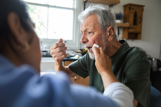 Caregiver helping senior man eat at home kitchen