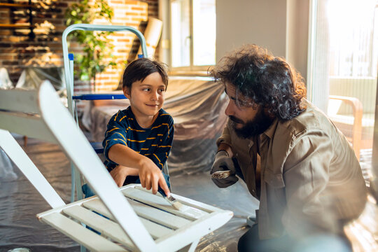 Father and son painting wooden chair at home