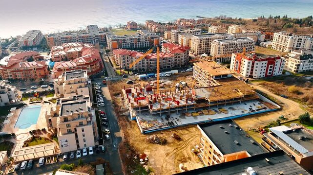Wide aerial panorama of coastal city construction and sea. View of building site surrounded by finished residential blocks