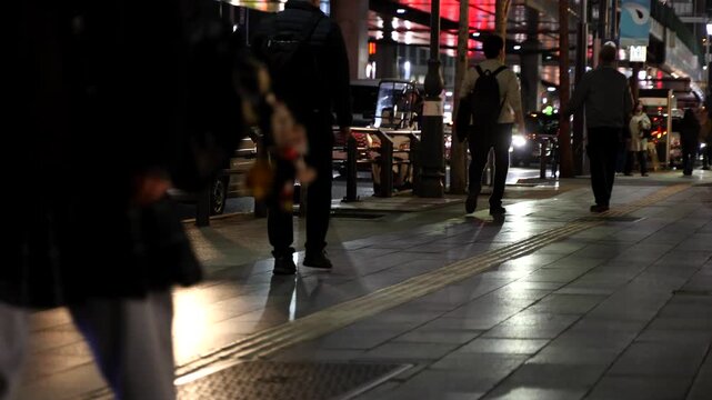 People walking in front of wooden vertical slats wall with warm lighting, urban lifestyle scene captured in real time. Ideal for business, lifestyle and modern city background footage.