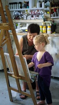 Child painting with an grandmother in a cozy art studio. Candid indoor moment of creativity and learning. Artistic lifestyle scene with real people and natural light.