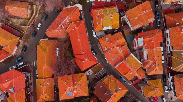 Top down aerial view of red tile rooftops in old town. Orange clay tile roofs, narrow streets, and parked cars in a historic European district.
