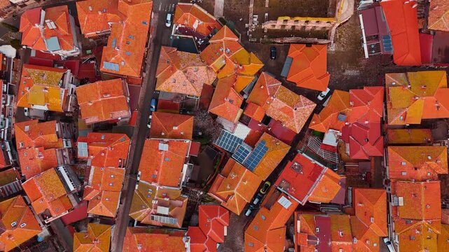 Vertical aerial view of dense orange rooftops and solar panels. Top down drone photography of historic buildings with clay tile roofs and modern solar panels on one rooftop.