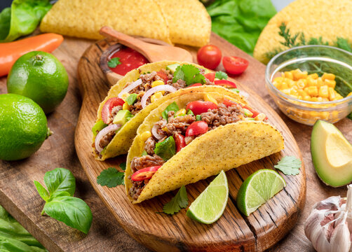 Mexican meat tacos or beef stuffed tortillas and lime slices near them on wooden serving board.