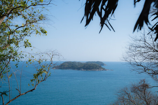 Tropical Puh island and smaller nearby island appearing through framing tree branches, offering a distant view of the calm, deep blue Andaman Sea under a clear sky
