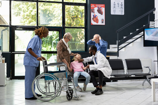 Elderly grandparents worried and shocked after child collapses at hospital, calling for immediate attention and first aid from medical team during pediatric health scare in waiting area.