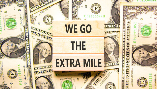 Support, help we go the extra mile symbol. Concept words We go the extra mile on beautiful wooden blocks. Beautiful dollar bills background. Business we go the extra mile concept. Copy space.