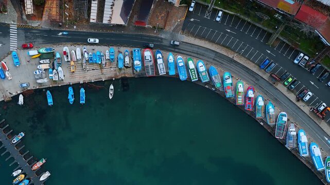 Top down view of fishing boats in harbor. Directly overhead shot of colorful fishing boats lined up at a concrete pier next to a road.