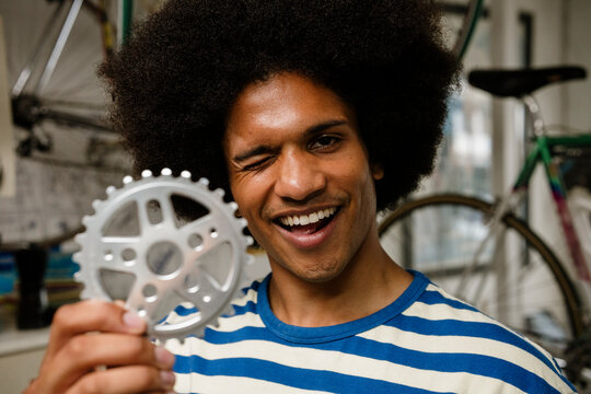 Happy urban bicycle mechanic winking holding gear in workshop