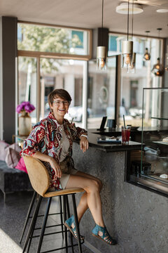Smiling woman sitting at cafe bar counter with drink during daytime