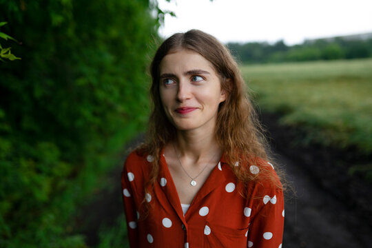 Woman with curly hair in red blouse standing in nature