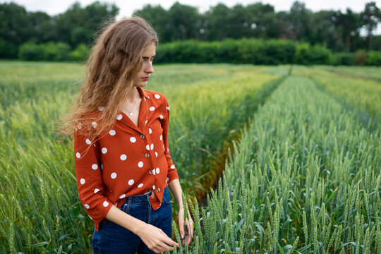 Smiling woman with curly hair in red blouse standing in wheat field