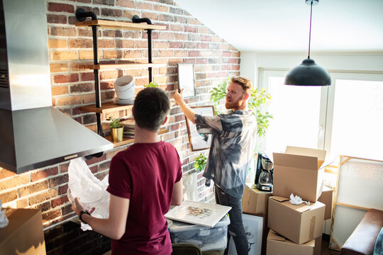Two men decorating kitchen while unpacking boxes at home