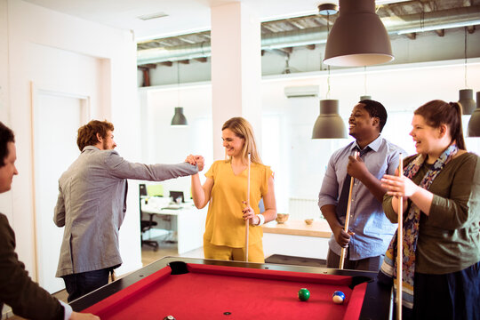 Coworkers playing pool in modern office break room