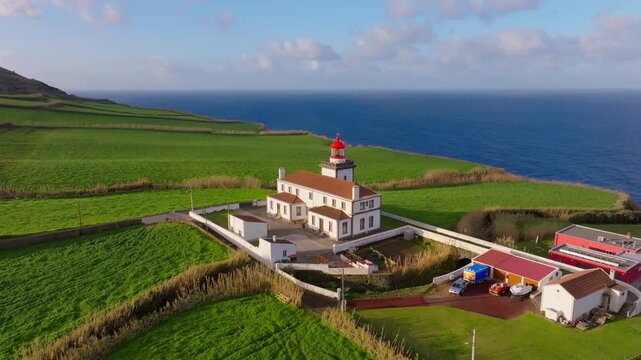 Aerial view of Farol da Ponta do Arnel lighthouse perched on a lush green cliff above the deep blue Atlantic Ocean in the Azores, Portugal.