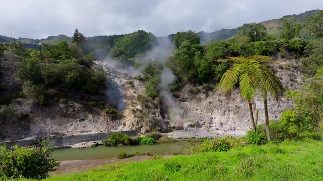 Aerial view of Furnas fumaroles where steam rises from geothermal vents, surrounded by dark rocks and contrasting volcanic textures in the Azores, Portugal.