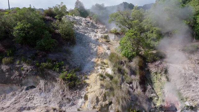 Aerial view of Furnas fumaroles where steam rises from geothermal vents, surrounded by dark rocks and contrasting volcanic textures in the Azores, Portugal.