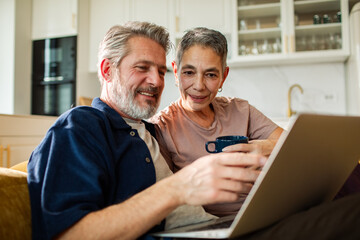 Smiling senior couple using laptop at home