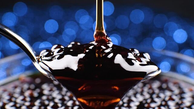 Dark boba pearls on spoon with pouring syrup and blue bokeh