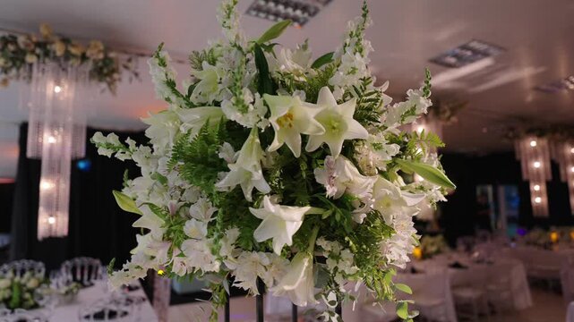 Refined wedding centerpiece with white Oriental lilies, stock flowers and soft filler florals complemented by greenery, styled for a luxury reception with elegant table decor and ambient lighting.
