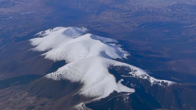 Elevated aerial view of the iconic Moncayo mountain covered by snow in sunny winter day, captured from an airplane cockpit flying at 8000m high