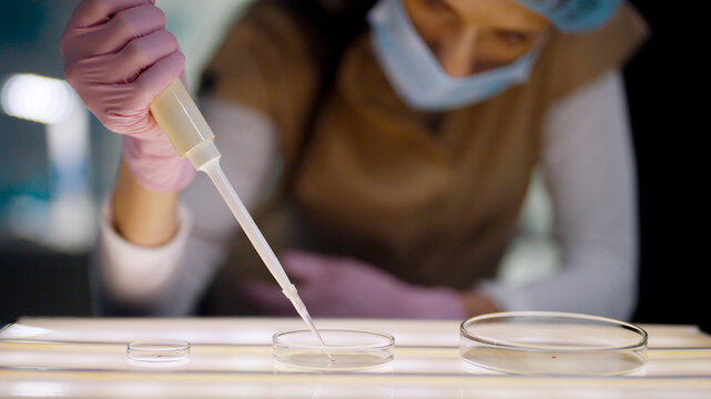 Female scientist in protective gear working in a modern laboratory to test human DNA samples. Preparing test samples with a pipette. Selective focus