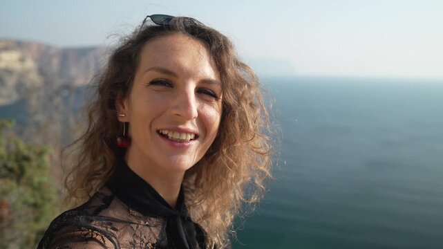 Woman blogger travel influencer enjoying scenic coastal views, recording a joyful vlog outdoors on a sunny vacation near the ocean cliff.