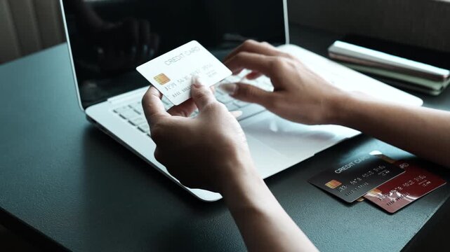 A woman holding a credit card while using a smartphone for online shopping, sitting at a desk with a laptop, representing digital payments and modern e-commerce lifestyle.