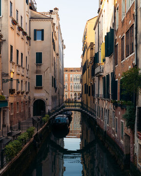 View of tranquil canal reflecting aged buildings and arched bridges, evoking the timeless charm of a Venetian waterway, Venice, Veneto, Italy.