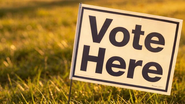 Pushing camera in while yard sign reading Vote Here swaying on wire stake in grassy lawn