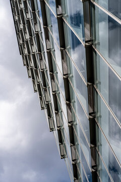 Contemporary glass office building facade with vertical perspective lines steel structure and windows reflecting clouds creating modern abstract city background