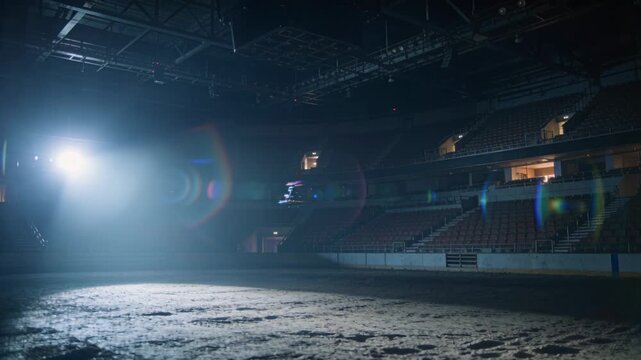 Activating overhead spotlight, lighting rig casting cone across arena floor, drone hovering inside