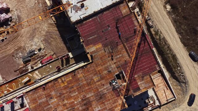 Workers are visible on the roof of a building under construction with cranes and construction materials scattered on the site during the late afternoon.