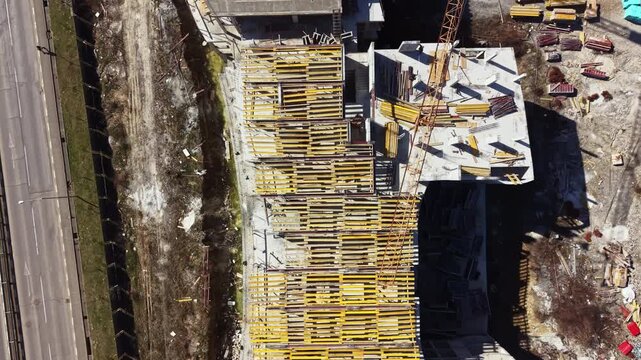 Workers are busy on a construction site with large wooden frameworks placed on top of the building. Tools and materials are scattered around as construction progresses.