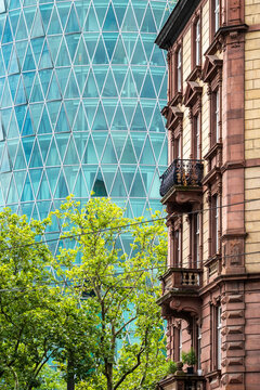 Architecture contrast in Frankfurt Bankenviertel Germany with historic facade balcony and trees against modern skyscraper diagrid skyline