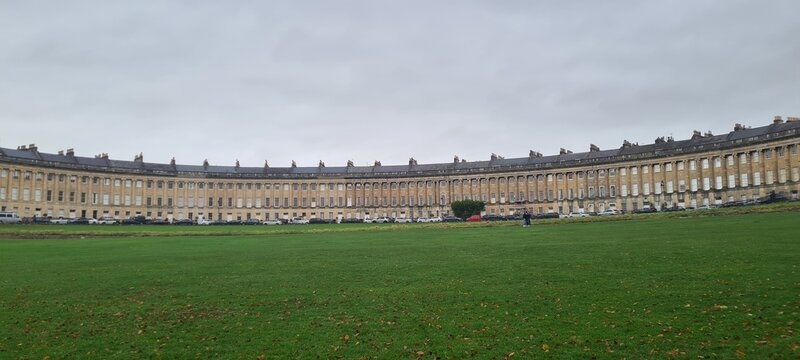 View of the elegant, curved facade of Royal Crescent buildings meeting the lush green lawn under an overcast sky, Bath, England, United Kingdom.