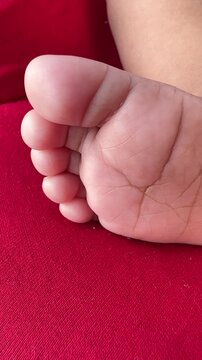 Close-up video of a newborn baby&rsquo;s soft foot resting on a red fabric surface, showing delicate skin texture and tiny toes. Warm natural lighting highlights innocence, comfort, and early childhood det