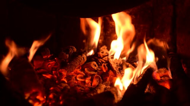 Close up of burning wood logs in a fireplace with bright orange flames and glowing embers