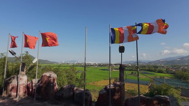 Daytime view from Tong Lam Son Temple overlooking Nha Trang, Vietnam. Vietnamese and Buddhist flags in the foreground, rice fields in the middle ground and the city skyline in the background 
