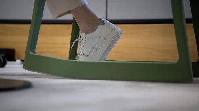 Close-up of foot rocking on a modern chair, conveying nervousness, tension and restlessness in a quiet office environment. Subtle fidgeting suggests anxiety or anticipation.