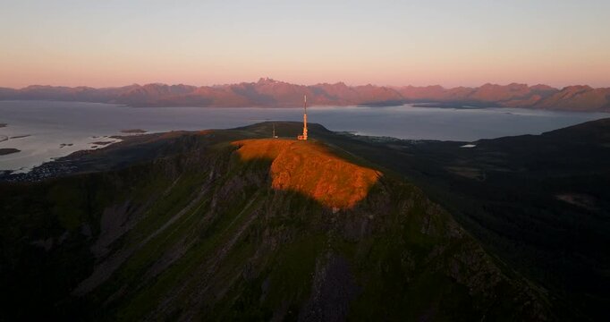 Cinematic aerial view, Storheia above Stokmarknes, Hadsel Municipality, northern Norway at sunset, revealing TV and radio tower, fjord water, and distant peaks