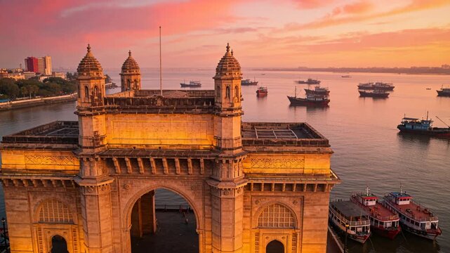 Pulling back drone capturing triumphal arch at waterfront quay, showing moored boats and flagpole