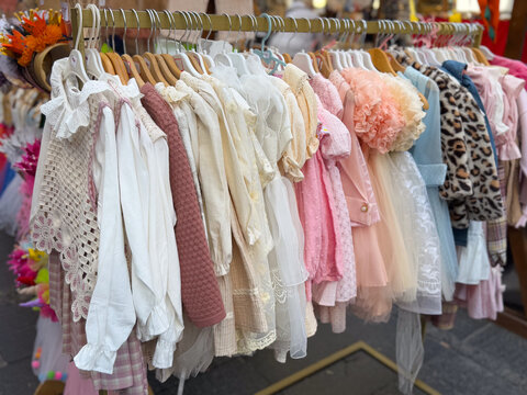 Boutique rack with elegant girls clothing in lace, tulle, and pastel fabrics at a market. Children fashion retail, occasion dressing, curated assortment, and premium textile presentation for festive